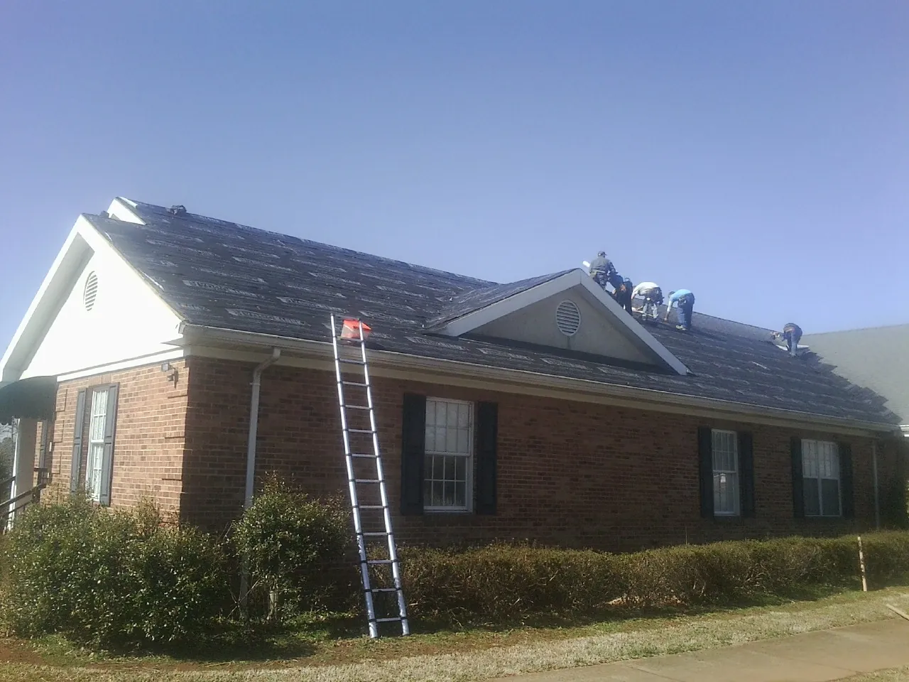 Crew tearing shingles off a brick ranch roof with a ladder set — Emergency Roof Repair work by our crew in Arlington